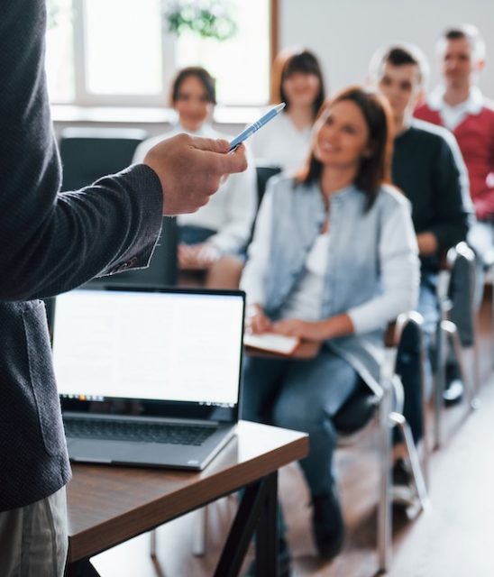Everyone is smiling and listens. Group of people at business conference in modern classroom at daytime.